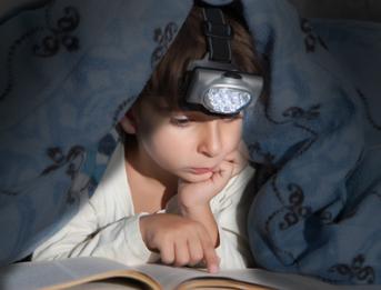 Kind liest im Dunkeln unter der BEttdecke