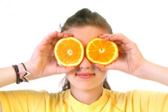 Vitamin C kann grauem Star vorbeugen. Kind mit Zitrone vor den Augen. 